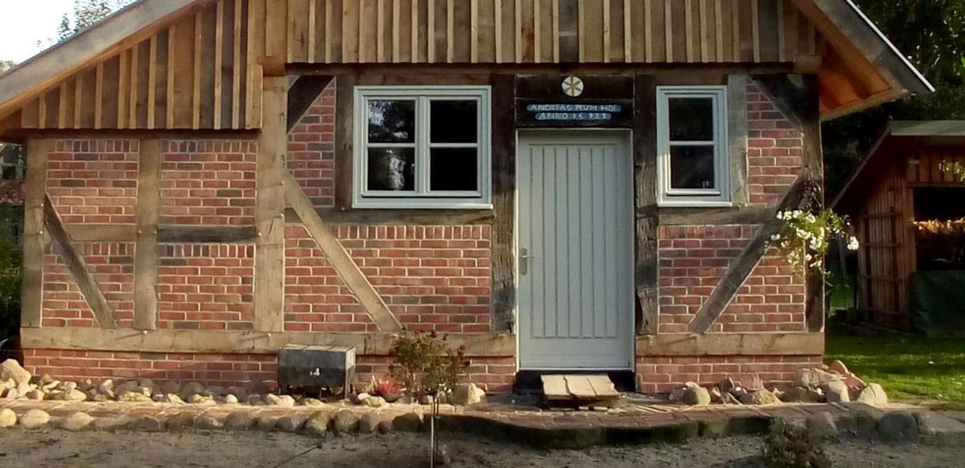 Die Front eines kleineren Fachwerkhauses ist mit einer Tür, sowie zwei kleinen Fenstern zu sehen.